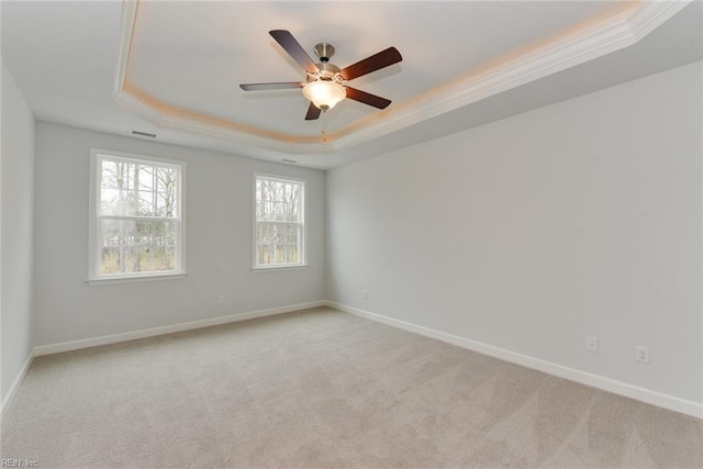 empty room featuring a raised ceiling, ceiling fan, crown molding, and light colored carpet