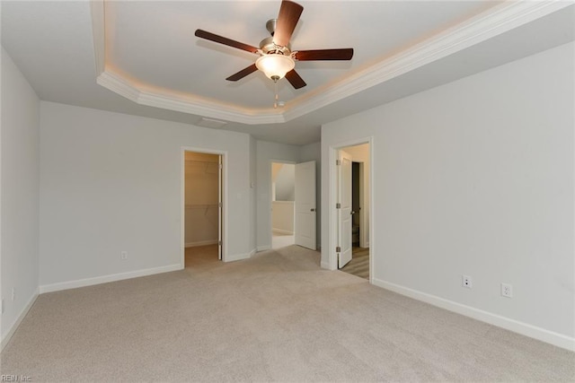 unfurnished bedroom featuring a closet, a raised ceiling, light colored carpet, ceiling fan, and a walk in closet