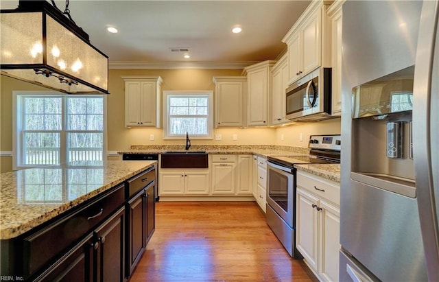 kitchen with light stone counters, ornamental molding, stainless steel appliances, light hardwood / wood-style floors, and white cabinetry