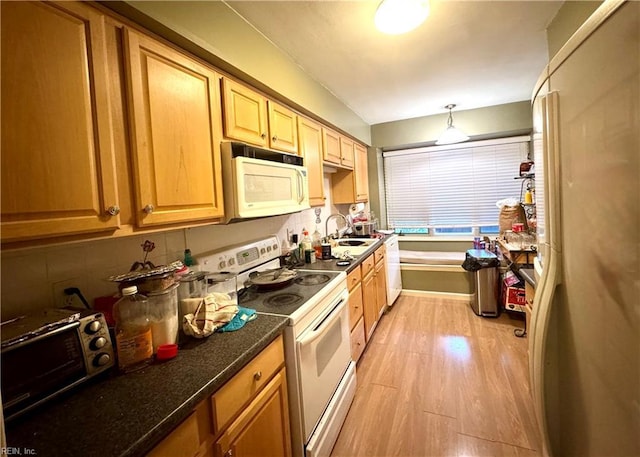 kitchen with sink, white appliances, dark stone countertops, light hardwood / wood-style flooring, and hanging light fixtures