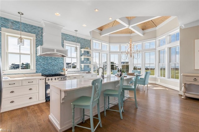 kitchen featuring a breakfast bar area, white cabinets, a center island with sink, and high end range