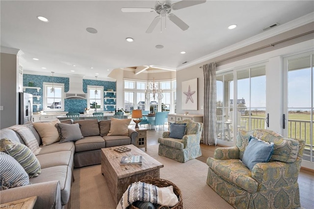 living room featuring light wood-type flooring, ceiling fan with notable chandelier, and crown molding