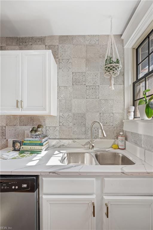 kitchen with light stone countertops, white cabinetry, sink, stainless steel dishwasher, and backsplash