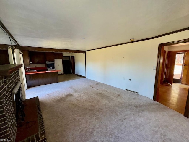 unfurnished living room with a brick fireplace, carpet floors, baseboard heating, and ornamental molding