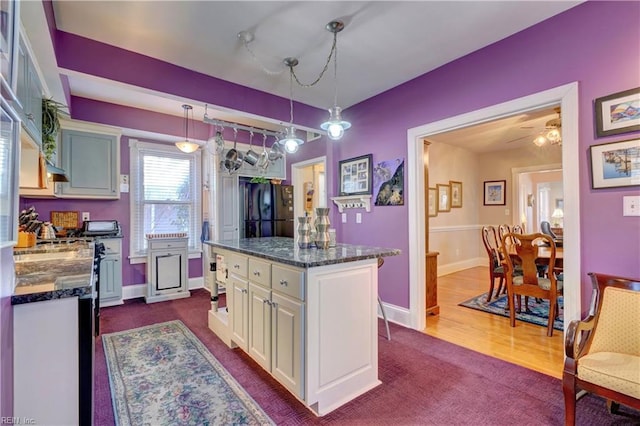 kitchen featuring black refrigerator, dark stone counters, ceiling fan, a center island, and hanging light fixtures