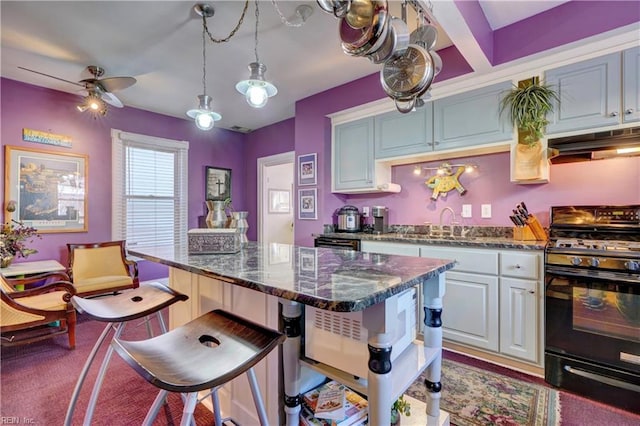 kitchen featuring a kitchen breakfast bar, ceiling fan, black gas range oven, decorative light fixtures, and a kitchen island