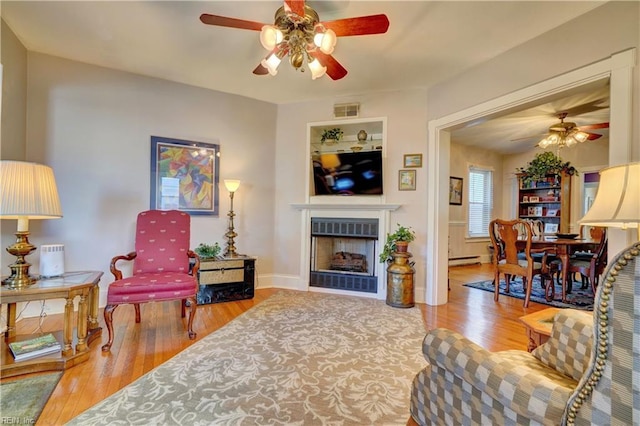 living room featuring ceiling fan, light hardwood / wood-style floors, and a baseboard heating unit