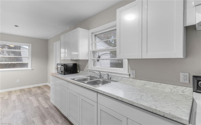 kitchen with light hardwood / wood-style floors, light stone counters, white cabinetry, and sink