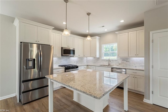 kitchen featuring hanging light fixtures, stainless steel appliances, a kitchen island, a kitchen bar, and white cabinets