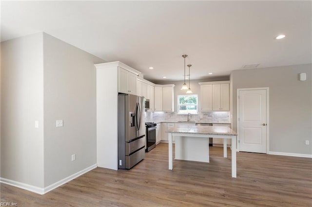 kitchen with decorative backsplash, stainless steel appliances, white cabinets, a kitchen island, and hanging light fixtures