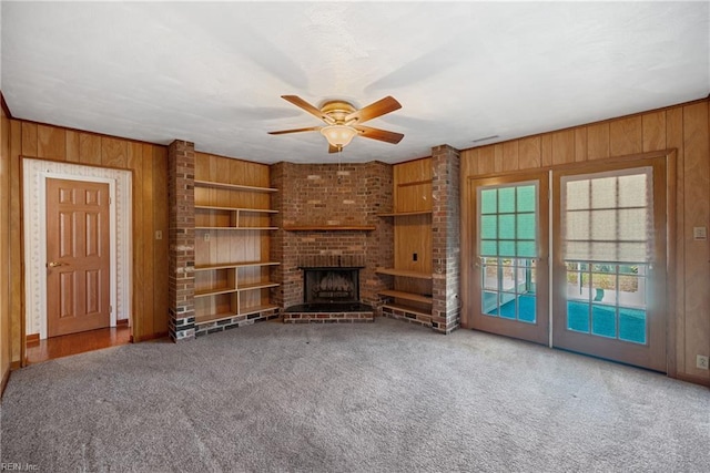 unfurnished living room with carpet, ceiling fan, a fireplace, and wood walls