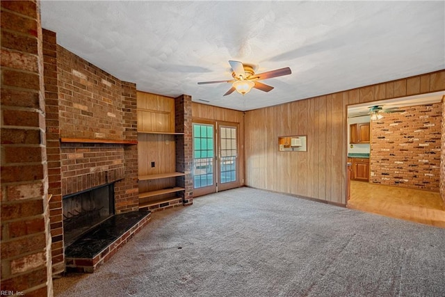 unfurnished living room featuring carpet flooring, ceiling fan, wood walls, and a fireplace