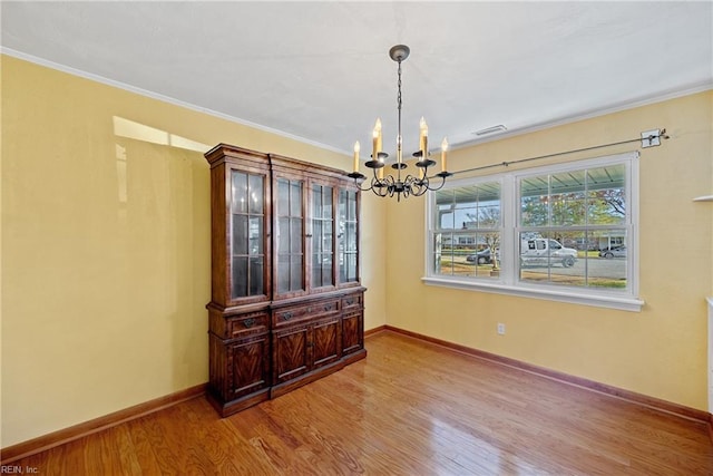 dining space with wood-type flooring, ornamental molding, and a notable chandelier