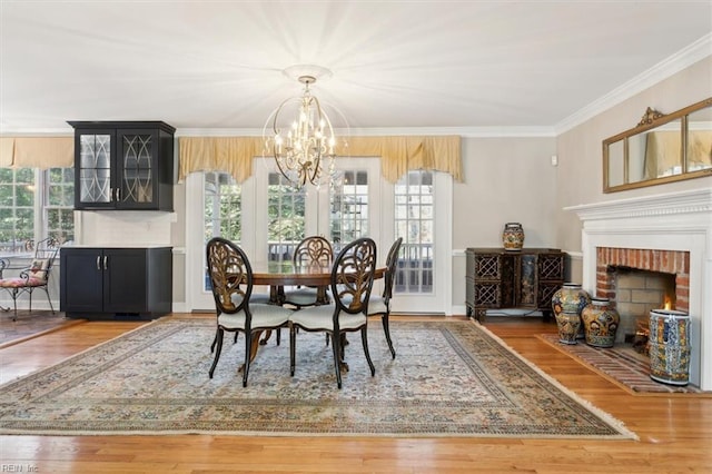 dining area with hardwood / wood-style flooring, ornamental molding, a fireplace, and an inviting chandelier