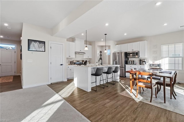 kitchen featuring stainless steel appliances, an island with sink, white cabinetry, and a breakfast bar area