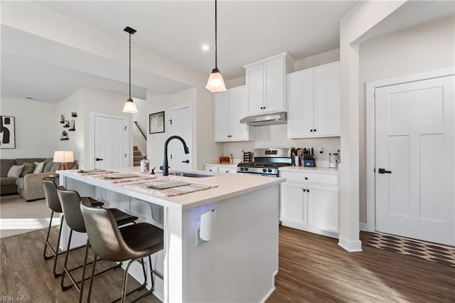 kitchen with sink, white cabinetry, an island with sink, stainless steel gas range oven, and hanging light fixtures