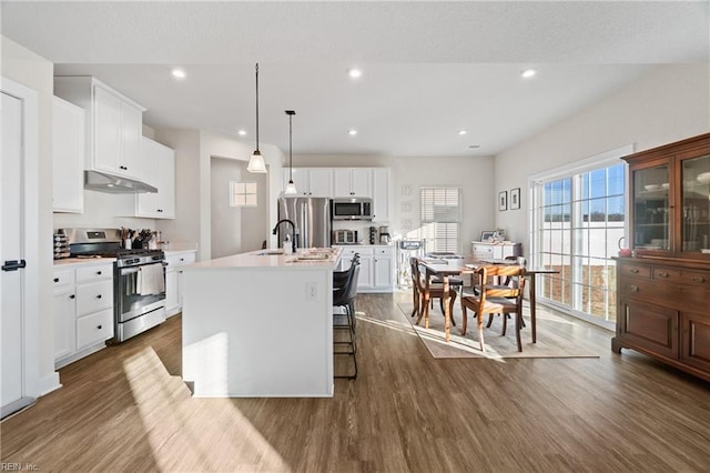 kitchen featuring a breakfast bar area, a center island with sink, appliances with stainless steel finishes, pendant lighting, and white cabinetry