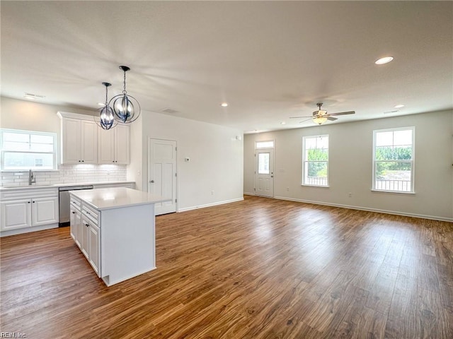 kitchen with decorative backsplash, stainless steel dishwasher, ceiling fan with notable chandelier, a kitchen island, and white cabinetry