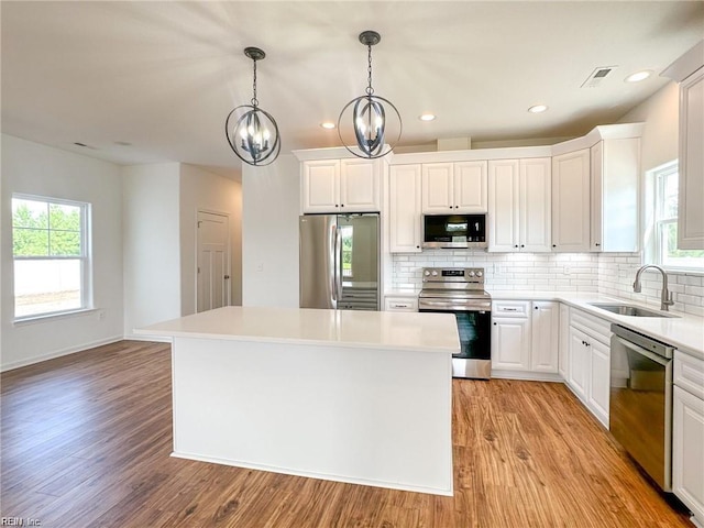 kitchen with an inviting chandelier, white cabinets, sink, a kitchen island, and stainless steel appliances