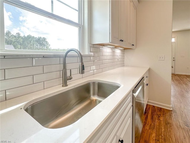 kitchen with dark hardwood / wood-style flooring, backsplash, stainless steel dishwasher, sink, and white cabinets