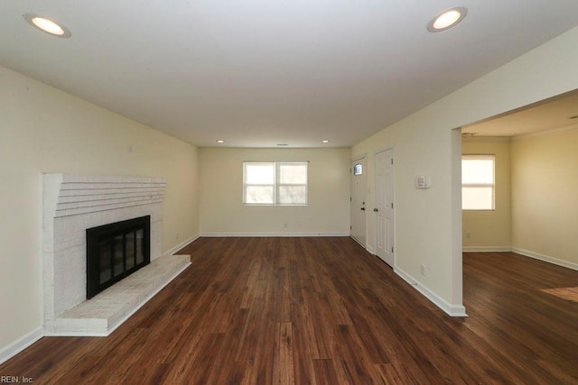 unfurnished living room featuring a wealth of natural light, dark hardwood / wood-style floors, and a brick fireplace