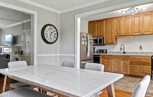 kitchen with sink, tasteful backsplash, light stone counters, appliances with stainless steel finishes, and ornamental molding