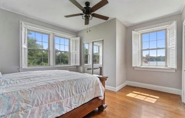 bedroom featuring multiple windows, radiator, light wood-type flooring, and ceiling fan