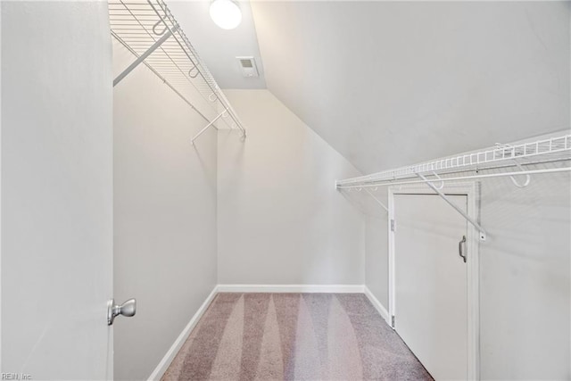 walk in closet with light colored carpet and vaulted ceiling