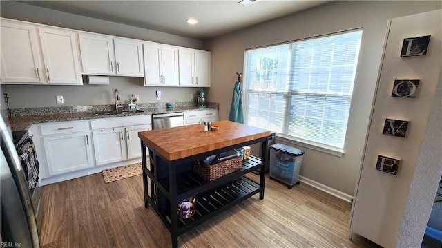 kitchen featuring butcher block counters, sink, light hardwood / wood-style flooring, stainless steel dishwasher, and white cabinets