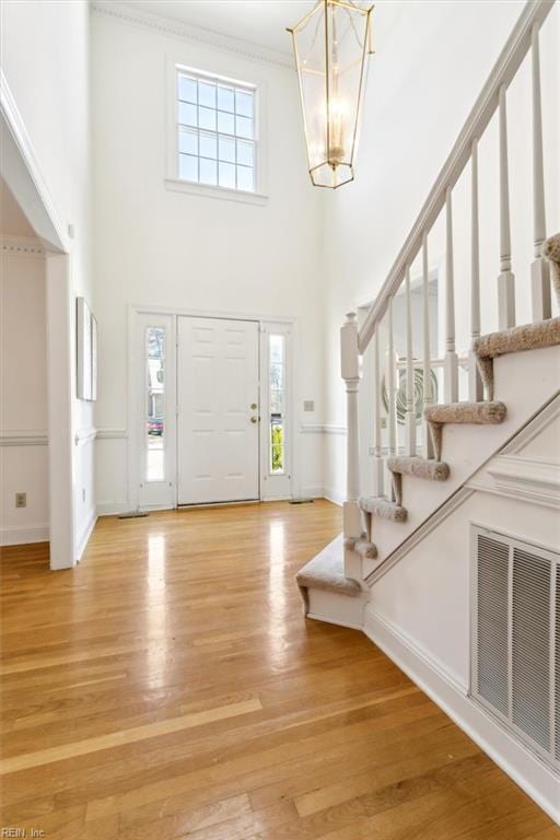 foyer with a high ceiling, light wood-type flooring, crown molding, and a notable chandelier