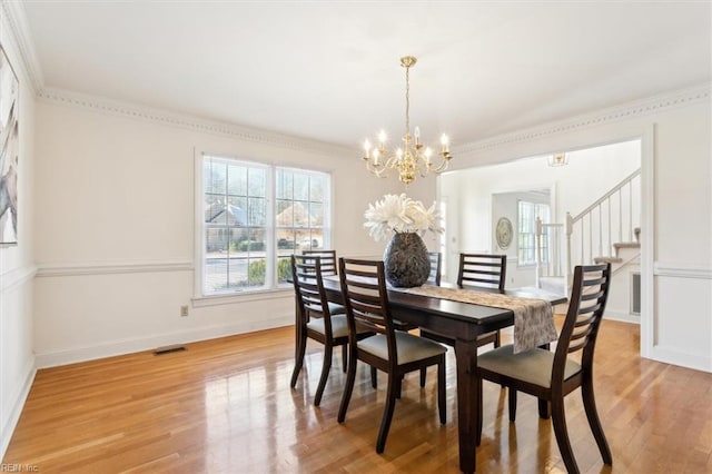 dining area with light hardwood / wood-style floors, ornamental molding, and an inviting chandelier