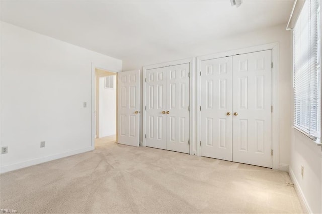 unfurnished bedroom featuring two closets and light colored carpet