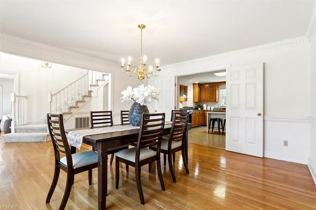 dining area with ornamental molding, light wood-type flooring, and a notable chandelier