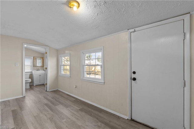 unfurnished bedroom with ensuite bathroom, a sink, a textured ceiling, light wood finished floors, and baseboards