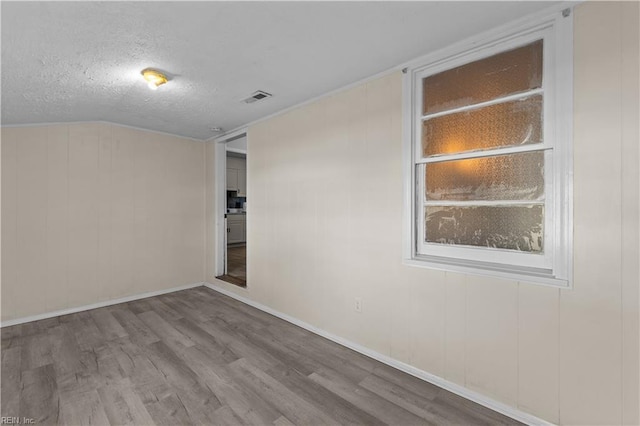 empty room with visible vents, baseboards, vaulted ceiling, wood finished floors, and a textured ceiling