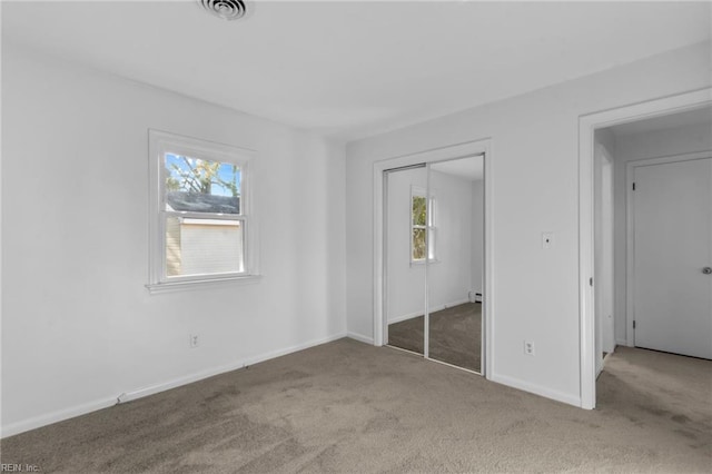 unfurnished bedroom with light colored carpet, a closet, and a baseboard heating unit