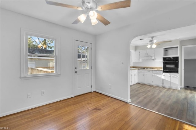 kitchen with black oven, white cabinetry, ceiling fan, and light wood-type flooring