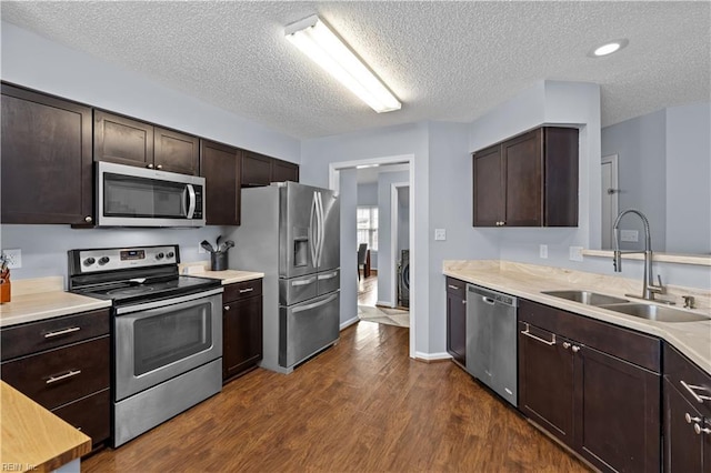 kitchen with appliances with stainless steel finishes, a textured ceiling, dark brown cabinetry, and sink