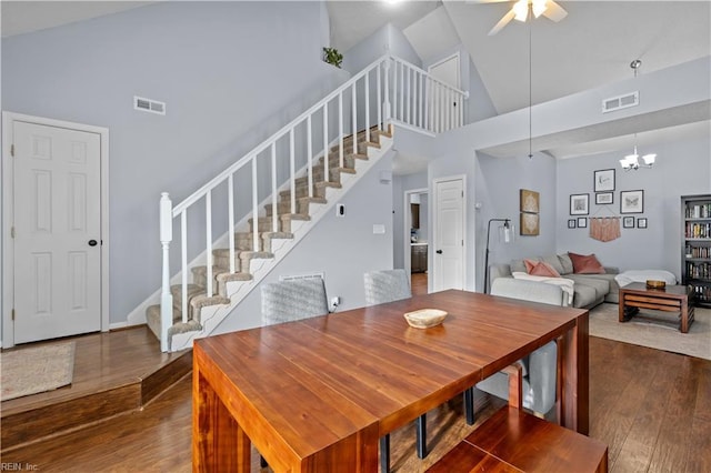 dining space with high vaulted ceiling, dark wood-type flooring, and ceiling fan with notable chandelier