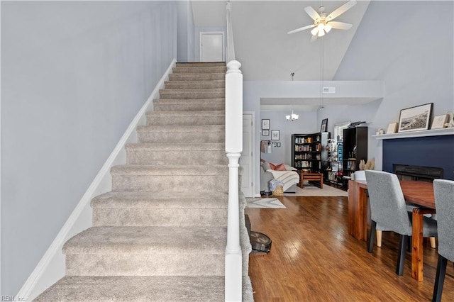 stairway with high vaulted ceiling, wood-type flooring, and ceiling fan with notable chandelier