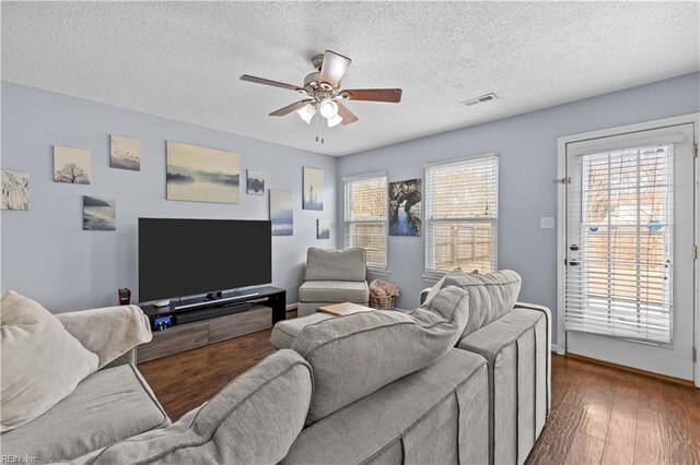 living room with a textured ceiling, plenty of natural light, dark wood-type flooring, and ceiling fan