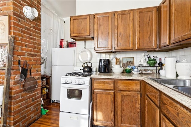 kitchen featuring dark hardwood / wood-style floors, white appliances, brick wall, and tasteful backsplash