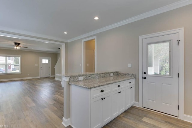 kitchen featuring white cabinets, kitchen peninsula, light stone countertops, and crown molding