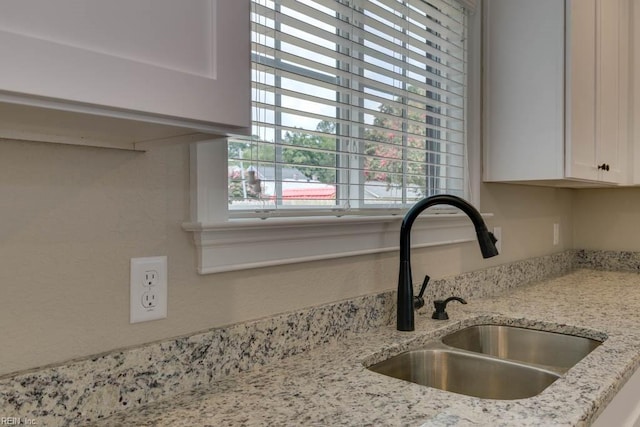 interior details featuring white cabinets, light stone counters, and sink