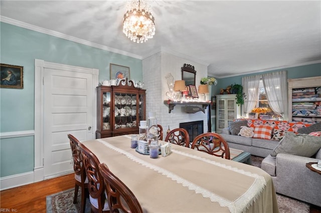 dining room featuring hardwood / wood-style floors, a large fireplace, an inviting chandelier, and ornamental molding