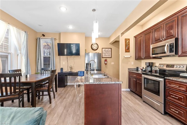 kitchen with sink, hanging light fixtures, stainless steel appliances, light hardwood / wood-style floors, and a center island with sink