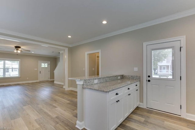 kitchen with white cabinets, light stone counters, kitchen peninsula, and ornamental molding