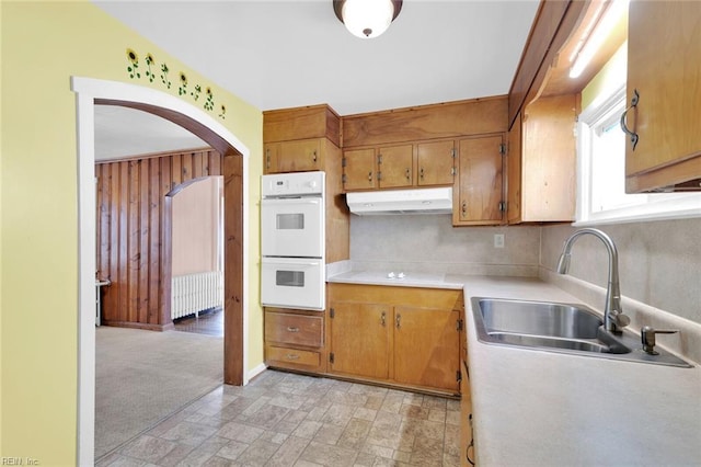 kitchen with radiator heating unit, light colored carpet, double oven, and sink