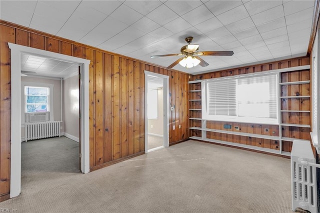 interior space with wood walls, light carpet, cooling unit, ceiling fan, and radiator heating unit