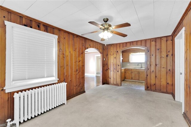 carpeted spare room with radiator heating unit, ceiling fan, and sink